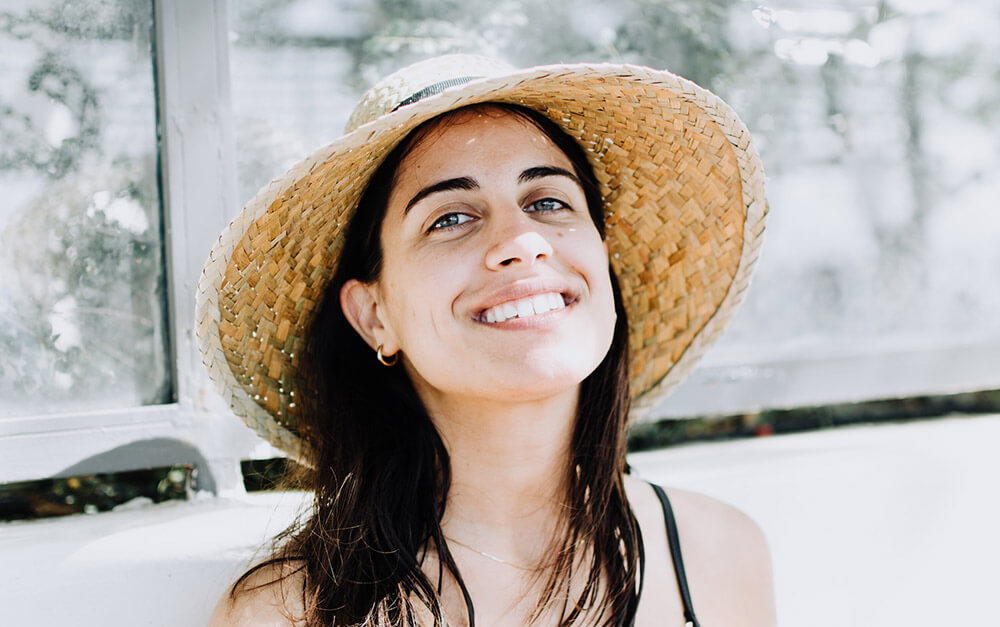 Close up photo of smiling woman wearing a straw hat and black top.