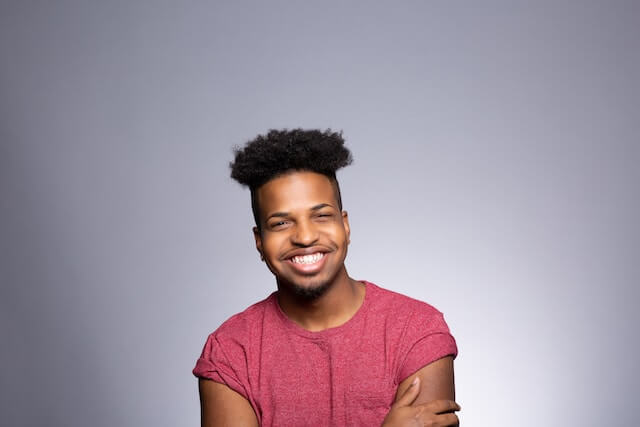 Photo of a smiling man with arms crossed in front of him wearing a red top in front of a blank grey backdrop.